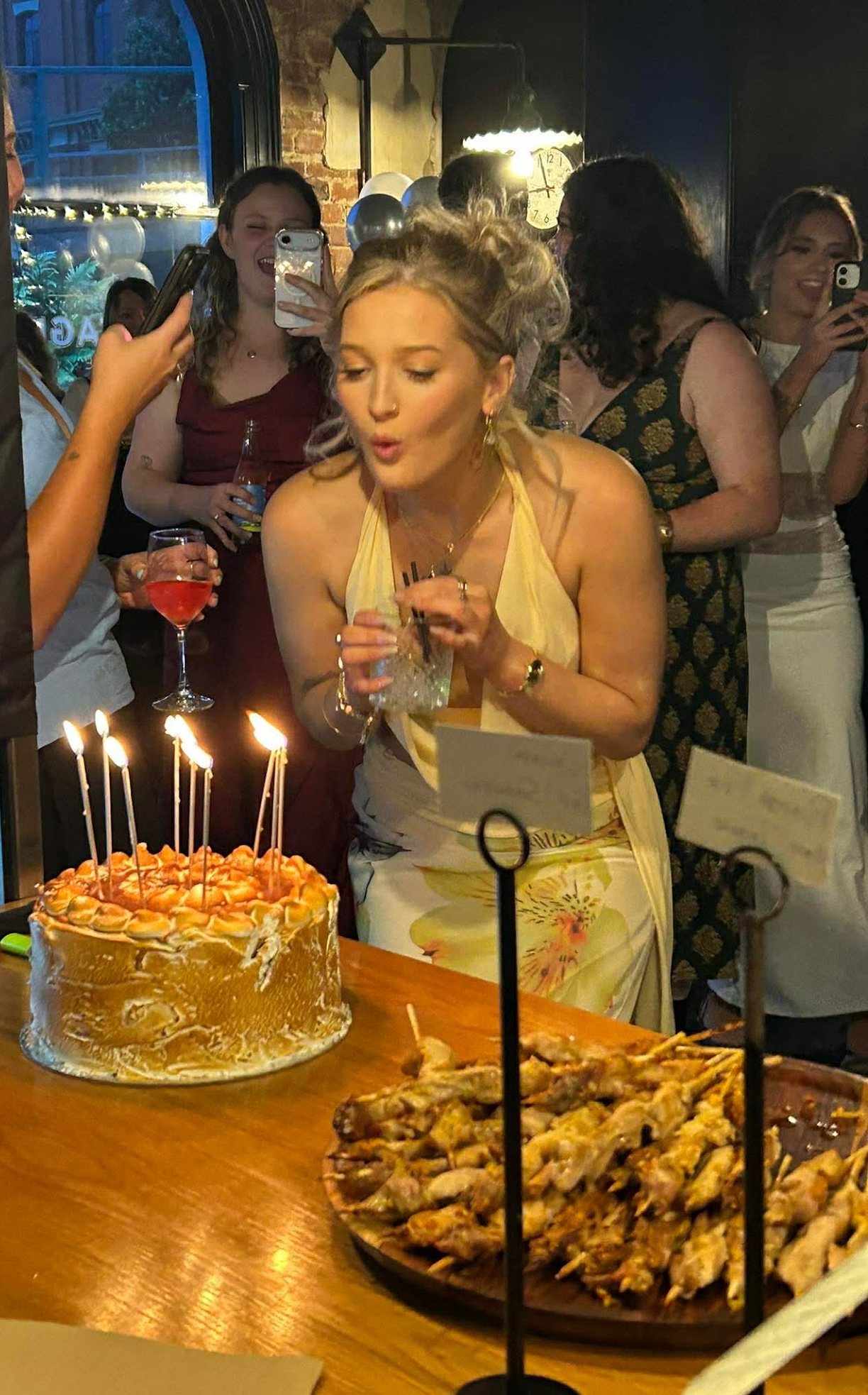 Blowing out the candles on a birthday cake at the bar, with a platter of satay from the kitchen alongside