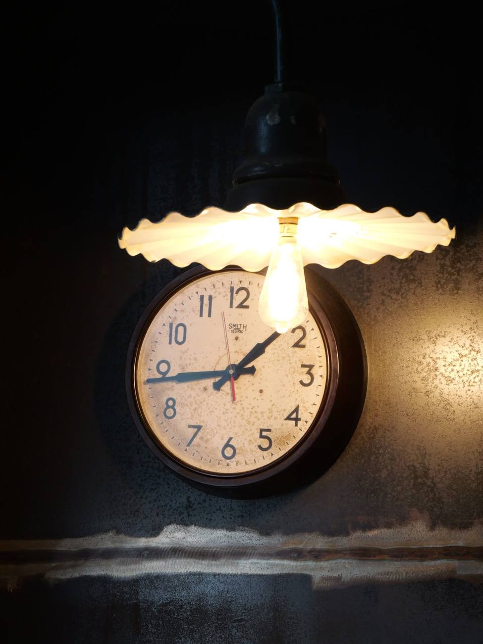 A clock and a pendant lamp against the old wall